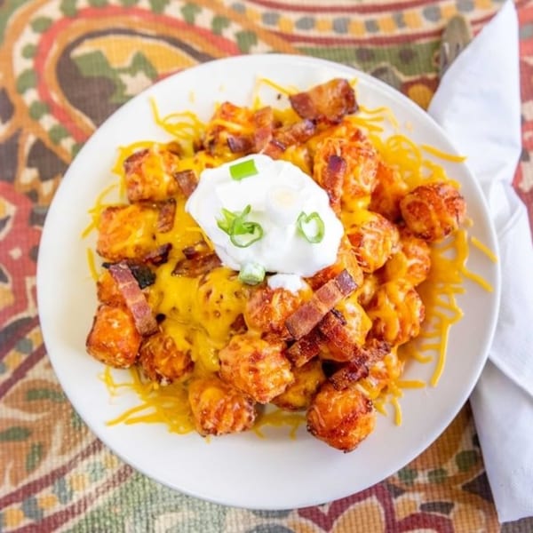 A plate of crispy tater tots covered in melted cheese, bacon bits, and a dollop of sour cream.