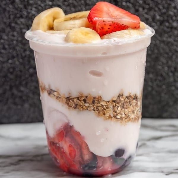 A clear cup of Breakfast Club yogurt parfait with layers of fruit, granola, and yogurt.