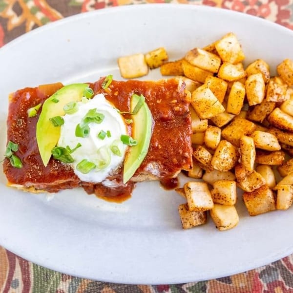 Breakfast Club enchilada with red sauce, avocado, sour cream, green onions, and a side of home fries.
